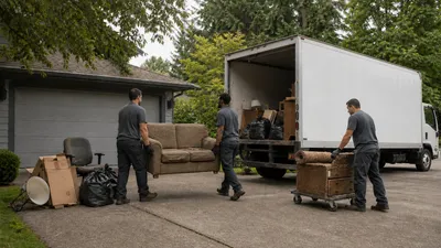 Two movers loading an old sofa and boxes into a junk removal truck